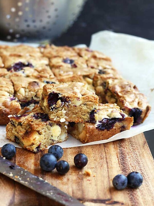 Blueberry, white chocolate & macadamia blondies on a wooden board and baking paper