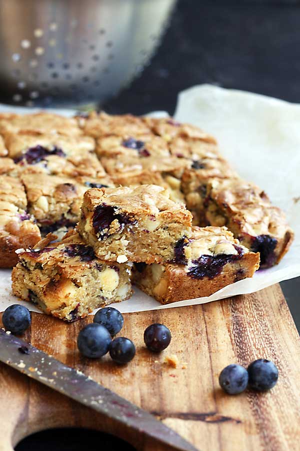 Blueberry, white chocolate &amp; macadamia blondies on a wooden board and baking paper