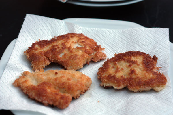 Pieces of crispy chicken for katsu chicken on kitchen paper and a white plate