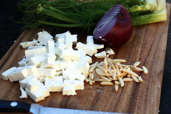 Cubes of feta and chopped almonds and other ingredients on a wooden chopping board for a blueberry, fennel and feta quinoa salad