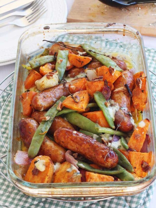 Sausage, sweet potato and orange traybake from above on a green and white checked cloth