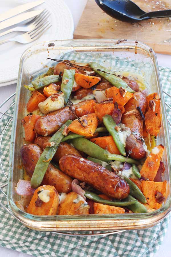 Sausage, sweet potato and orange traybake from above on a green and white checked cloth