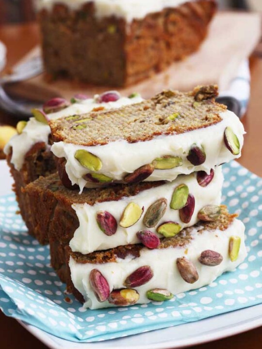 Pieces of banana and pistachio loaf stacked on a blue spotty cloth