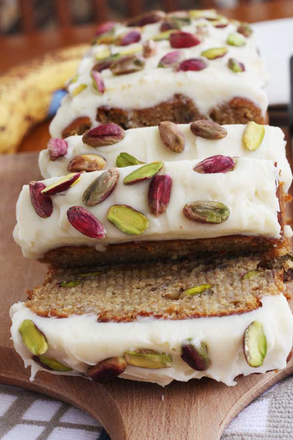 closeup of slices of banana and pistachio loaf with white chocolate cream cheese frosting