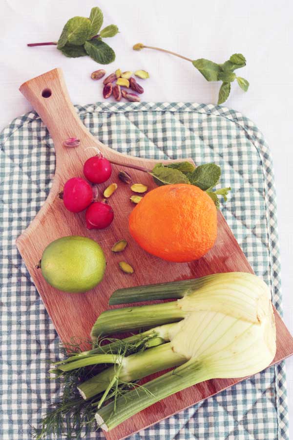 Blood orange and roasted fennel and radish salad ingredients on a wooden board and green checked place mat from above