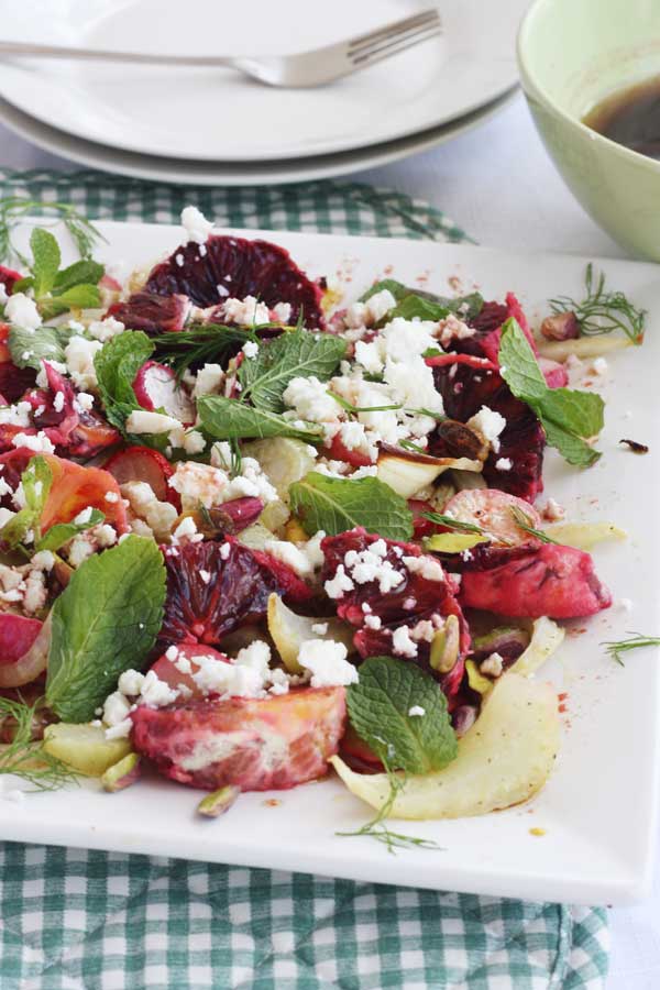 Closeup of a blood orange and roasted fennel and radish salad on a square plate with a checked mat under it