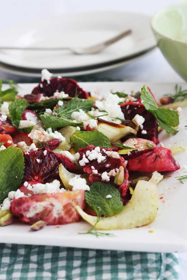 Closeup of a blood orange and roasted fennel and radish salad with white plates in the background