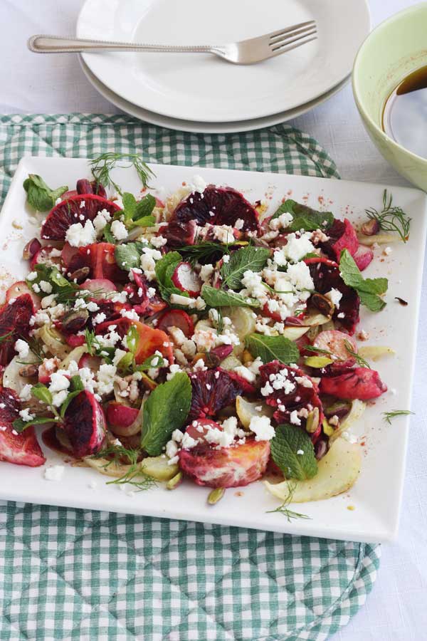 Blood orange and roasted fennel and radish salad on a square white platter and with a green checked placemat under it