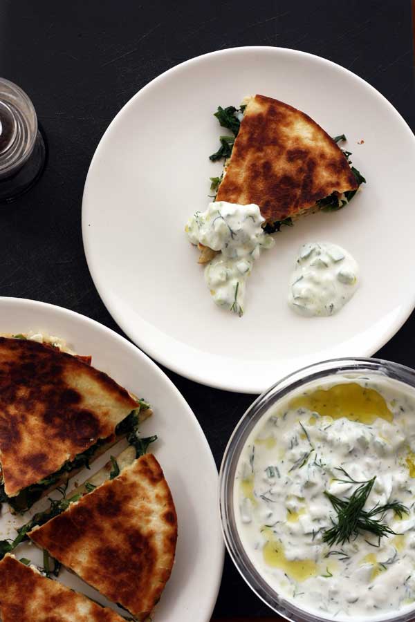A segment of Greek quesadilla on a plate with tzatziki and with a bowl of tzatziki to the side.