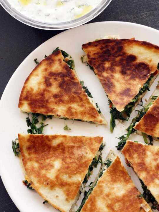 Greek quesadillas with tzatziki photographed from above on a big white plate and black background.
