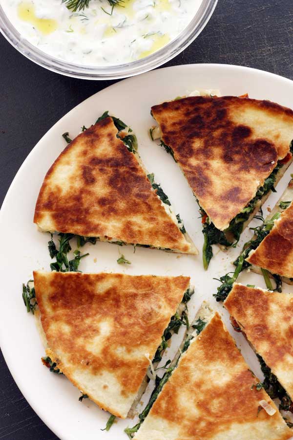 Greek quesadillas with tzatziki cut into slices on a white plate with a bowl of tzatziki on the side