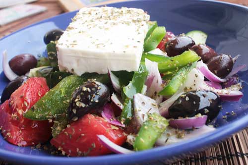 A colourful Greek salad in a blue bowl up close.