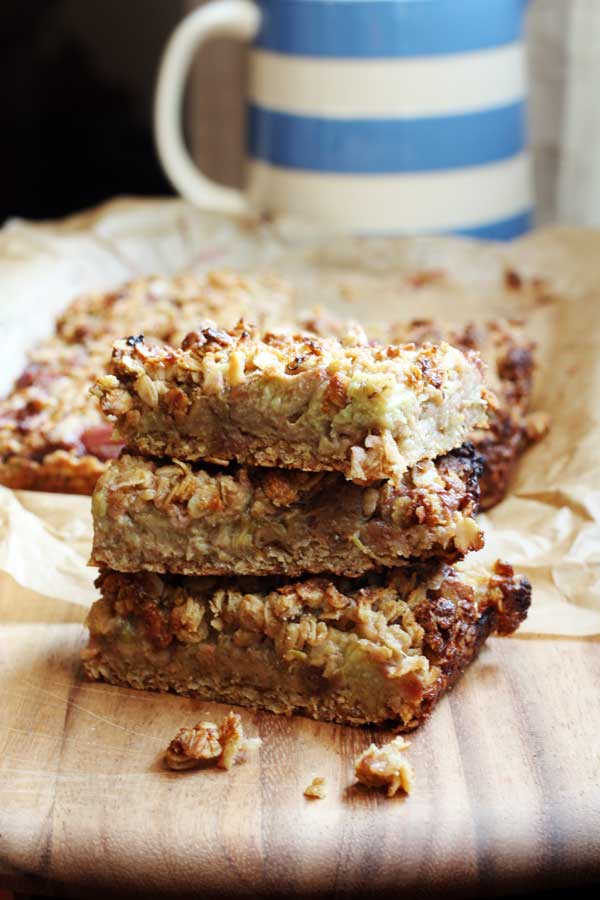 stack of 3 Healthy Oat Slices With Rhubarb And Ginger on a wooden board with a blue white striped jug in the background