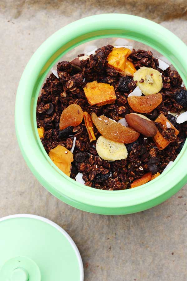 A container of tropical chocolate granola with a green rim on baking paper from above