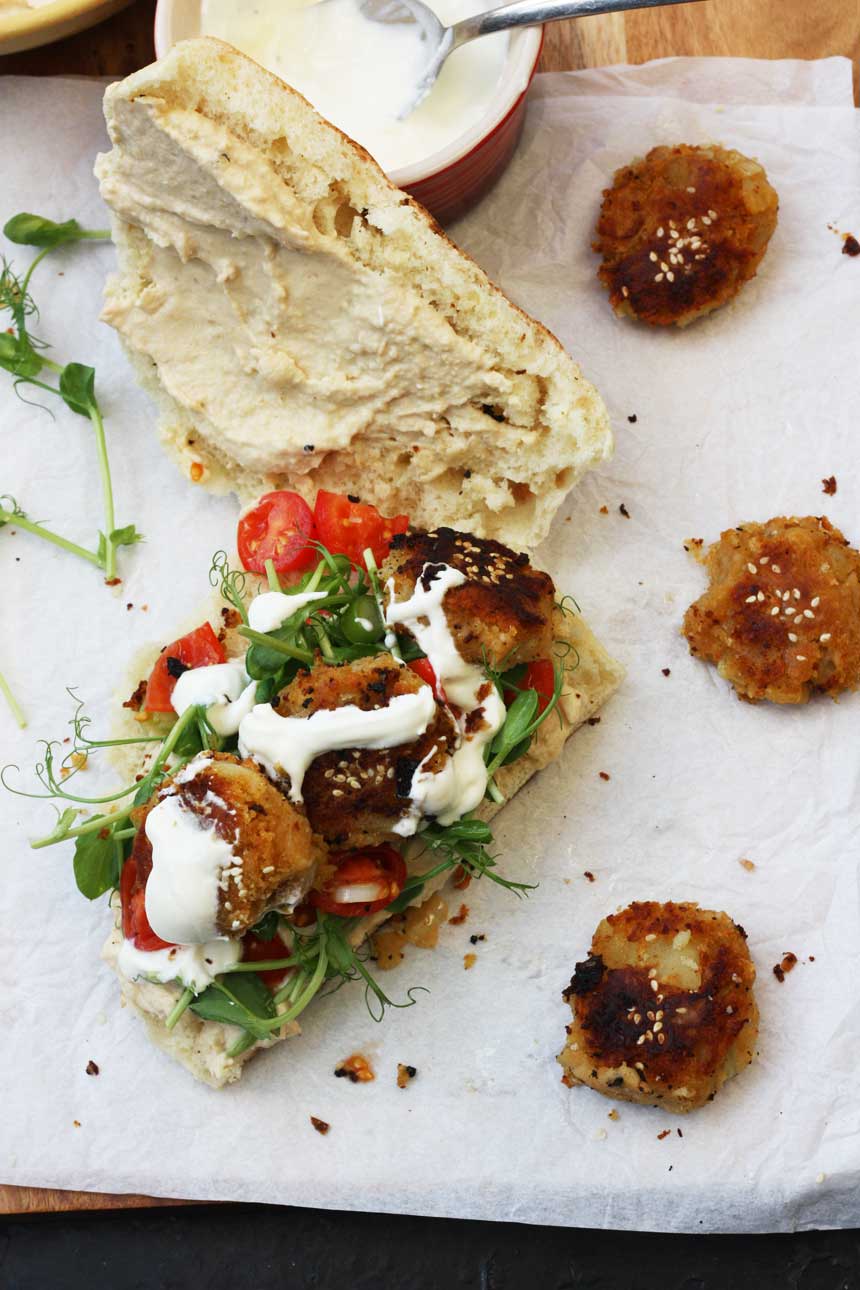 A roll with sweet potato falafel open on baking paper from above with more falafel scattered around.