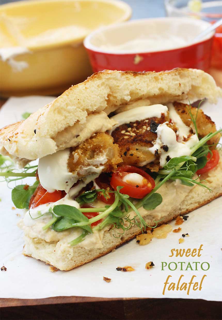 A sweet potato falafel sandwich from the side on baking paper with kitchen equipment in the background.