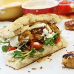 A sweet potato falafel sandwich from the side on baking paper with kitchen equipment in the background.