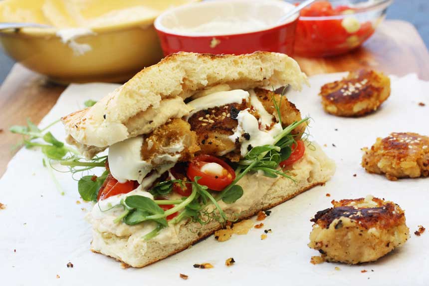 A sweet potato falafel sandwich from the side on baking paper with kitchen equipment in the background.