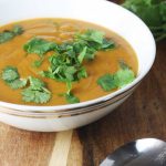 Crock pot Thai pumpkin and red lentil soup  in a white bowl on a wooden board and with a spoon