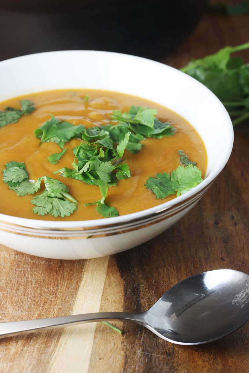 Crock pot Thai pumpkin and red lentil soup  in a white bowl on a wooden board and with a spoon