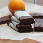 healthy chocolate orange date bars stacked on top of each other on baking paper with others around and an orange in the background.