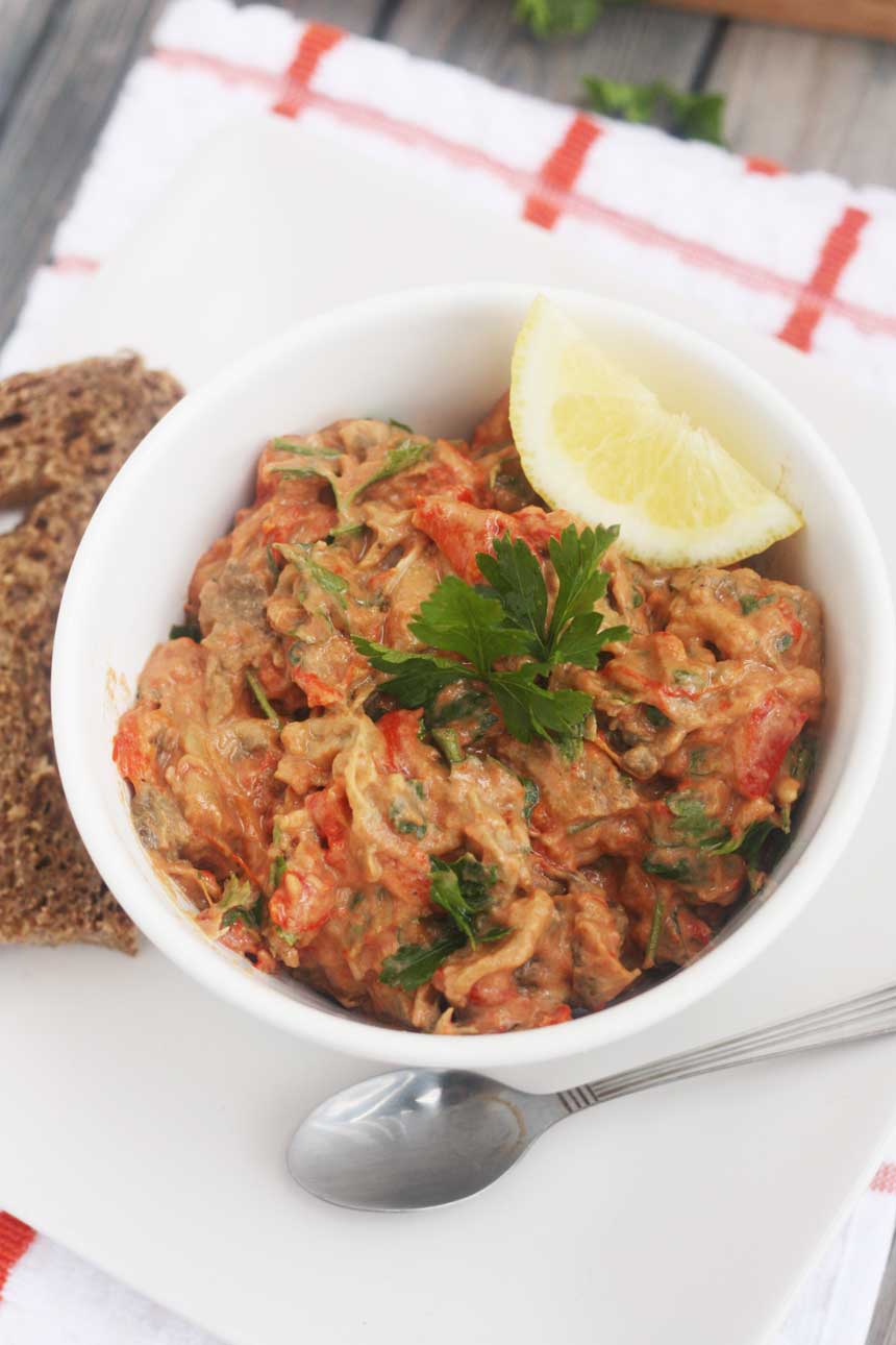 red pepper and eggplant plant dip in a small white bowl from above and on a red and white checked cloth