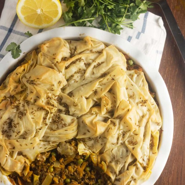 Overhead view of a samosa pie with a piece taken out in a white pie dish and on a wooden table.