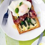 asparagus brunch tart with parmesan and basil with an egg on it on a white plate with a fork and on a green place mat.