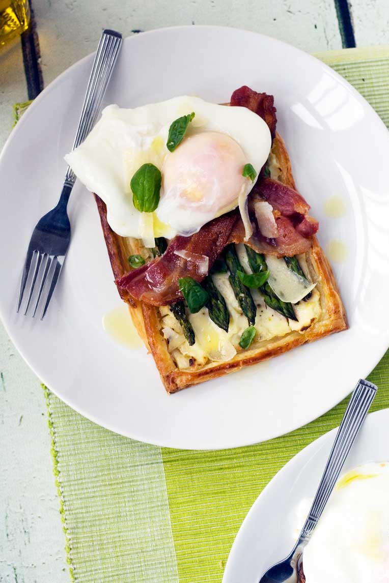 asparagus brunch tart with parmesan and basil with an egg on it on a white plate with a fork and on a green place mat.