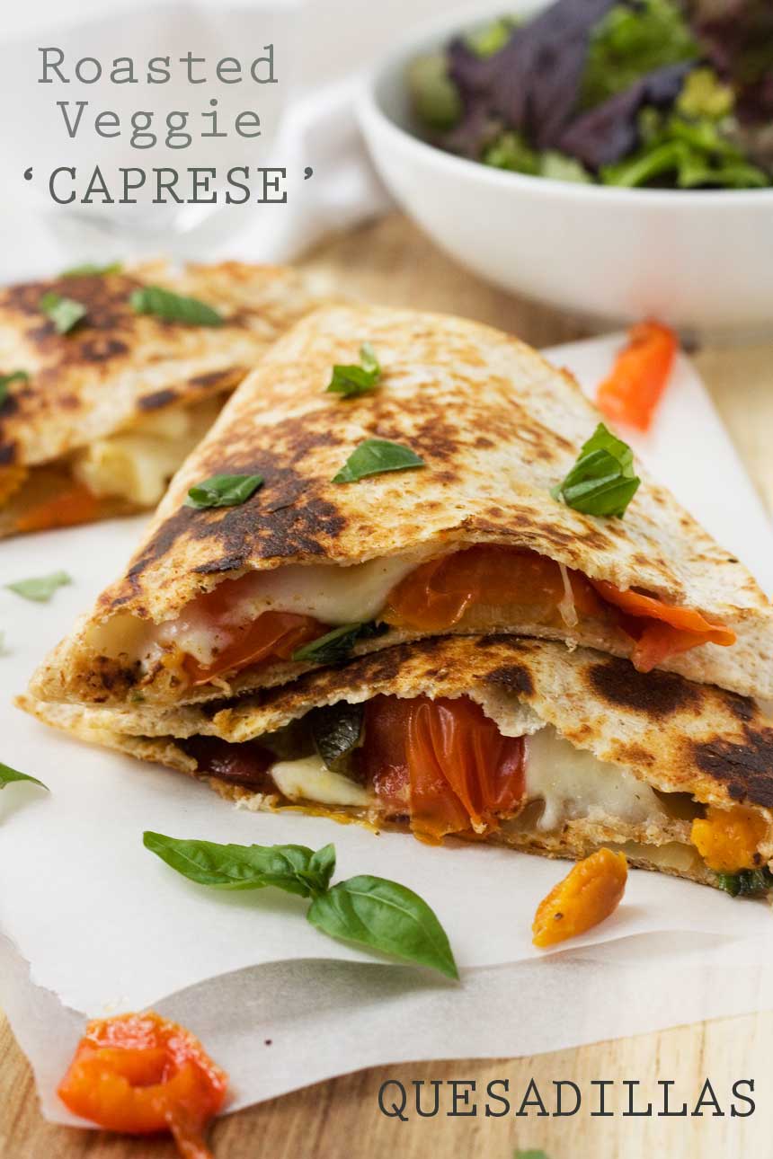 closeup of Caprese quesadillas stacked on top of each other on baking paper and a wooden board with a bowl of green salad.