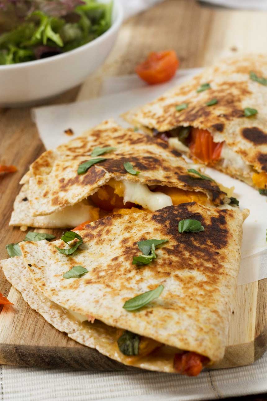 Roasted vegetable ‘caprese’ quesadillas on baking paper and a wooden board.