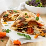 Caprese quesadillas stacked on top of each other on baking paper and a wooden board with a bowl of green salad.