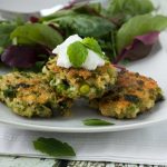 A small stack of pea, mint and feta quinoa fritters on a white plate with salad.