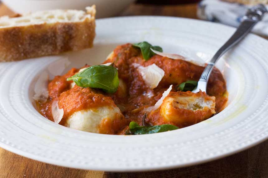 Ricotta gnudi with tomato sauce with a spoon in it in a white bowl.