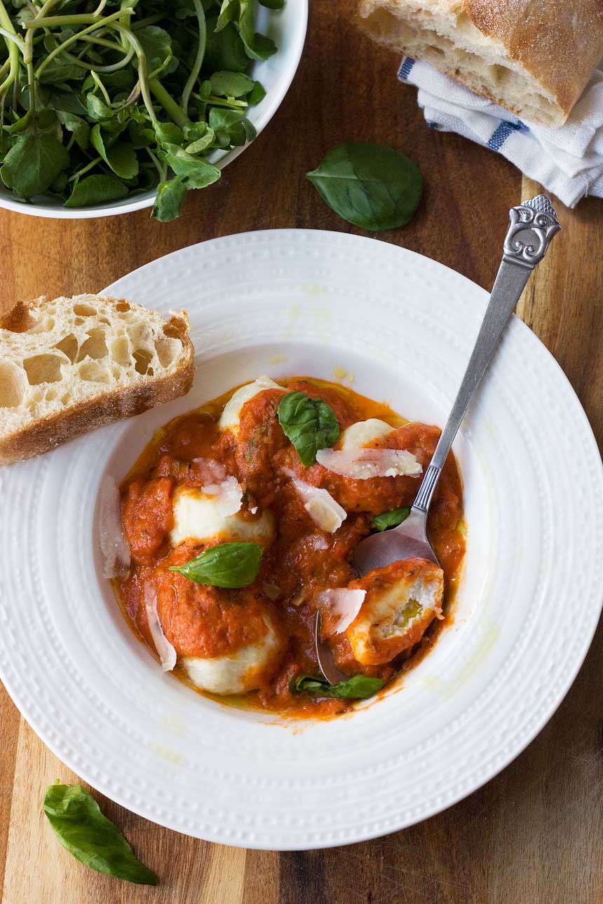 Ricotta gnudi photographed from above with a spoon in it and a piece of Italian bread on a wooden background.