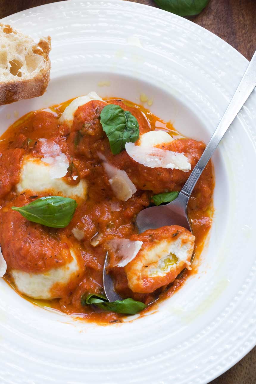 A white plate of ricotta gnudi pictured from above with a spoon in it.