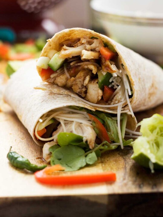 A hoi sin chicken noodle wrap cut in half and laying one half on top of the other on a wooden board.