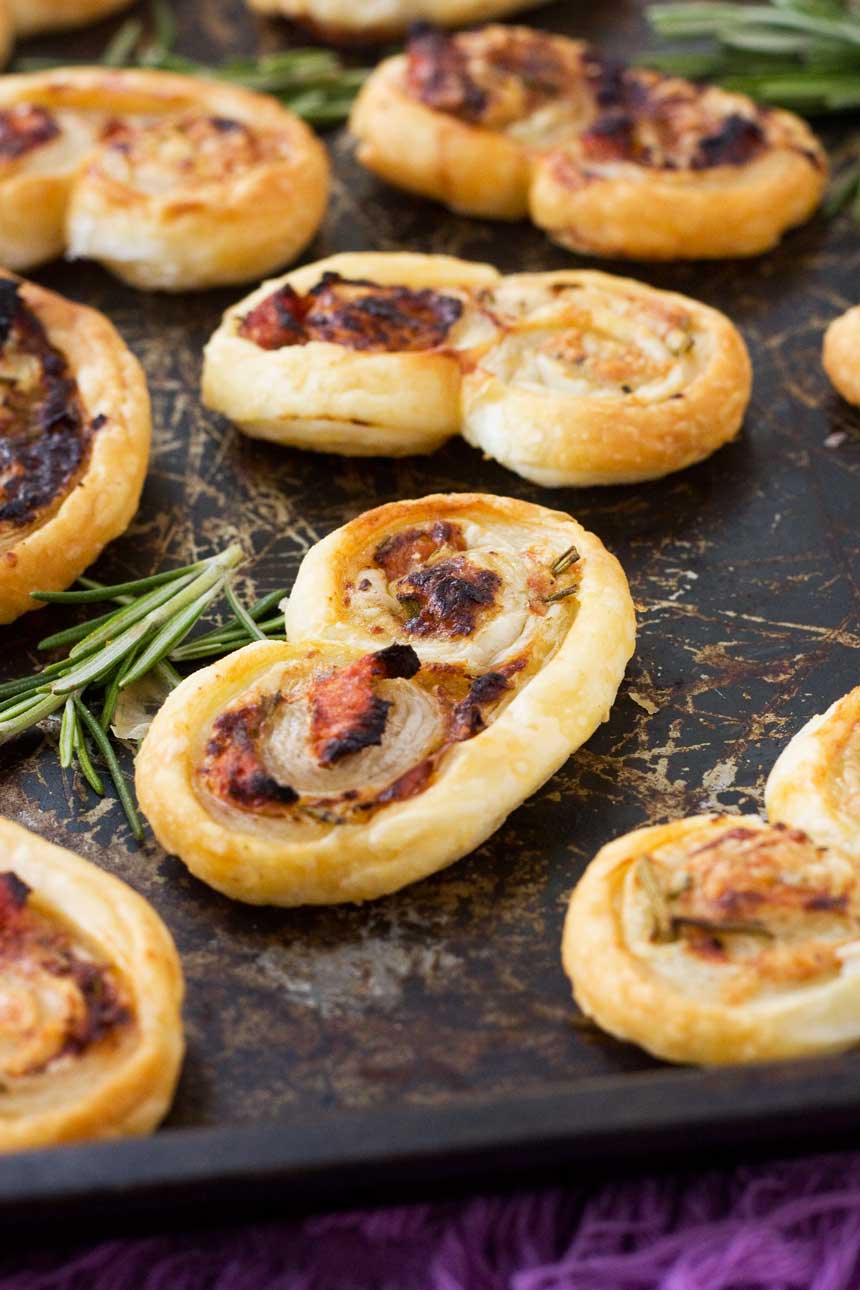 sun-dried tomato, parmesan and rosemary palmiers on a black baking tray with fresh rosemary.