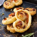 sun-dried tomato, parmesan and rosemary palmiers stacked up on a black baking tray.