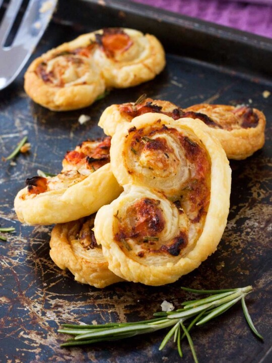 sun-dried tomato, parmesan and rosemary palmiers stacked up on a black baking tray.