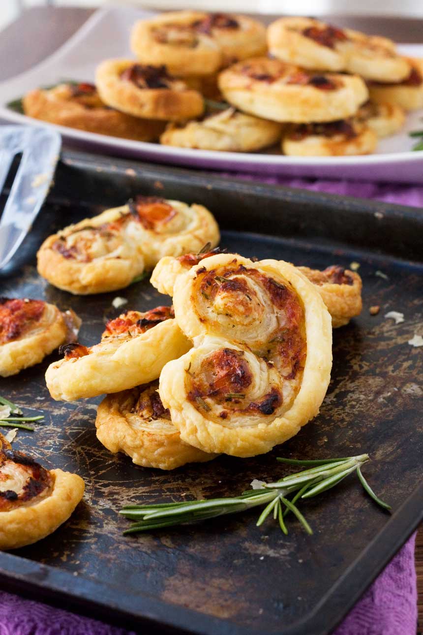 sun-dried tomato, parmesan and rosemary palmiers stacked up on a black baking tray.