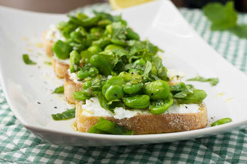 4 broad bean crostini on a rectangular white plate with a checked cloth underneath