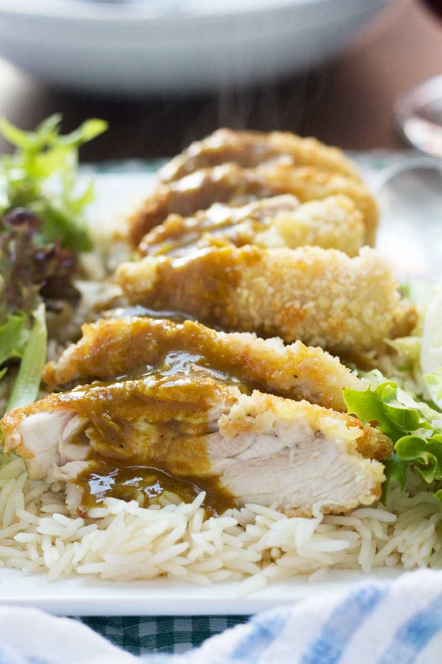 A close up of a chicken katsu with curry sauce meal on a bed of rice and lettuce