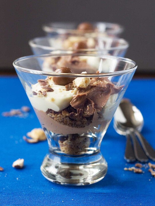 Chocolate malt cheesecakes in a glass on a blue background with spoons at the side.