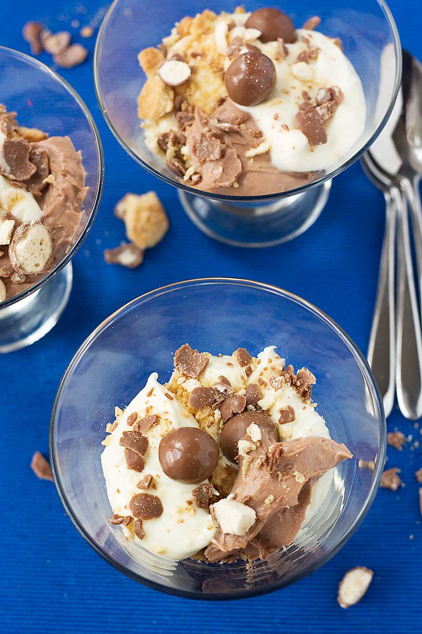 Chocolate malt cheesecakes in a glass on a blue background from above with spoons.