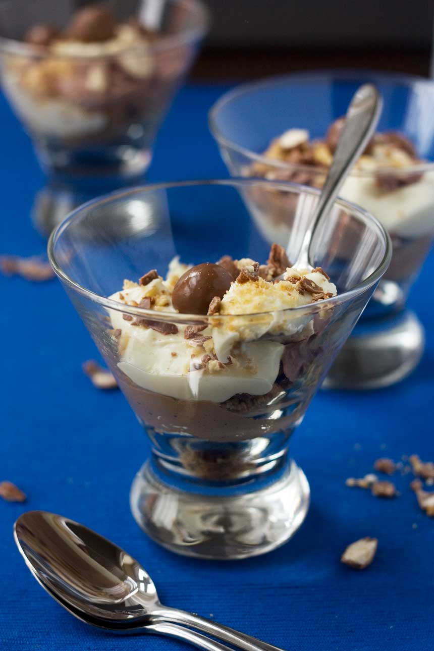 Chocolate malt cheesecake in a glass on a blue background with a spoon in it.