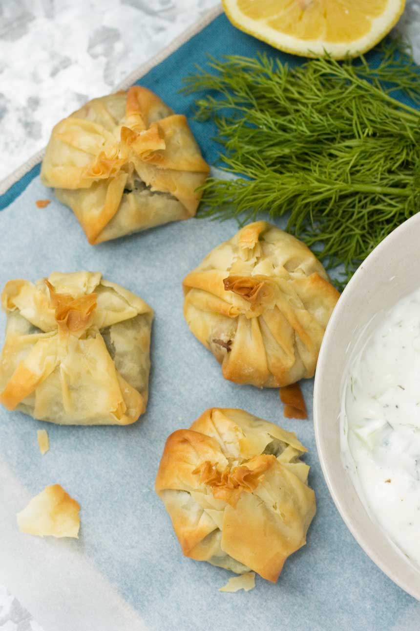 Greek filo parcels photographed from above with a bowl of tzatziki and dill.
