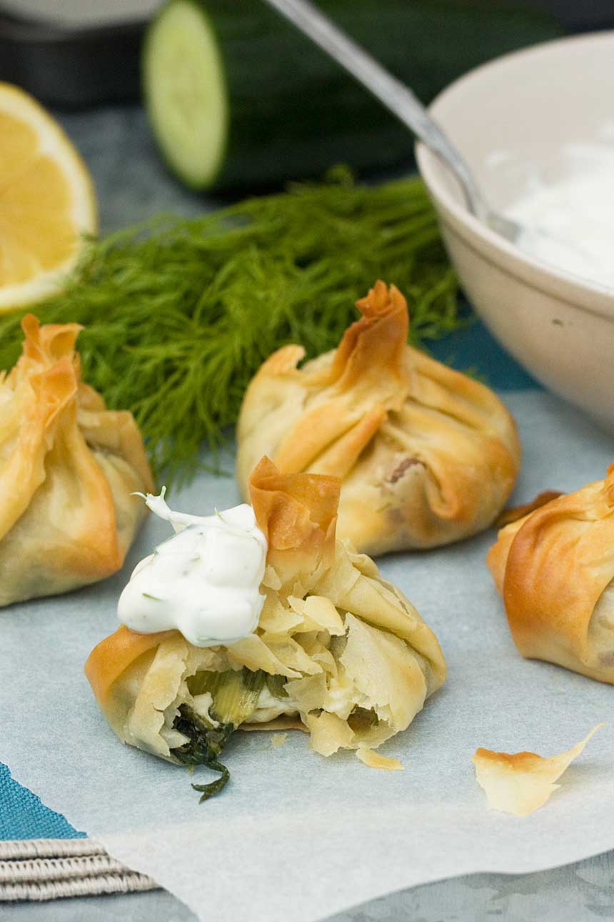 A Greek spinach and feta filo parcel with a bite out of it and tzatziki on top with others in the background