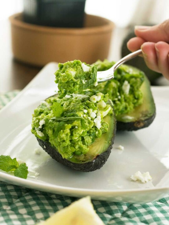 Someone eating Pea, mint and feta avocado boats on a white square plate.