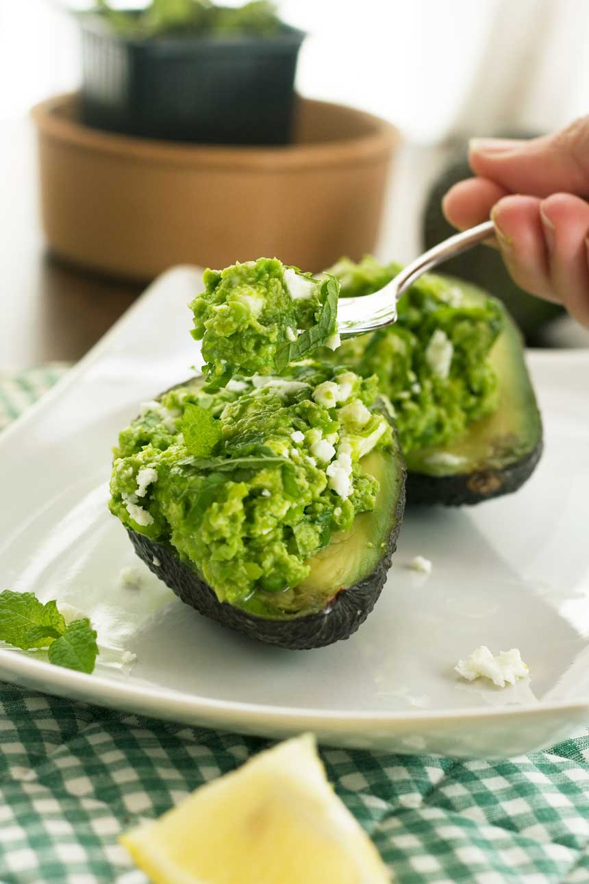 Someone eating Pea, mint and feta avocado boats on a white square plate.